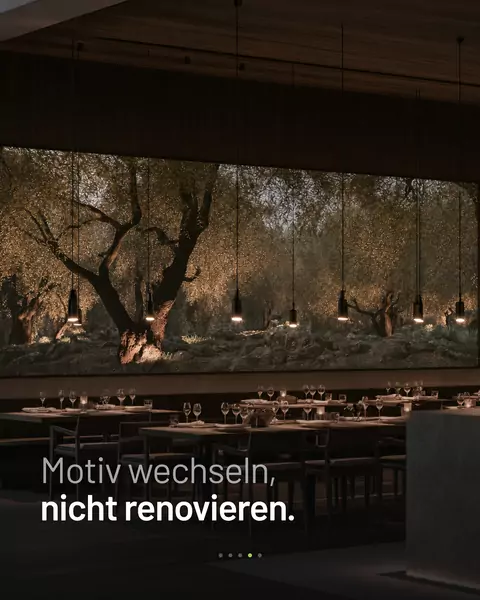 Feed-Slide: Restaurant mit einer leuchtenden Wand voller Olivenbäume, darüber „Motiv wechseln, nicht renovieren."