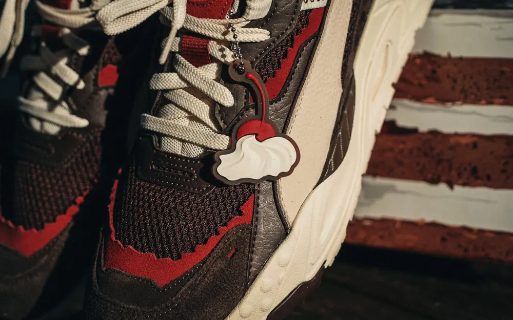 Nahaufnahme eines Sneakers vor der Tortenkante, am Schnürsenkel ein Anhänger in Form einer Sahnehaube